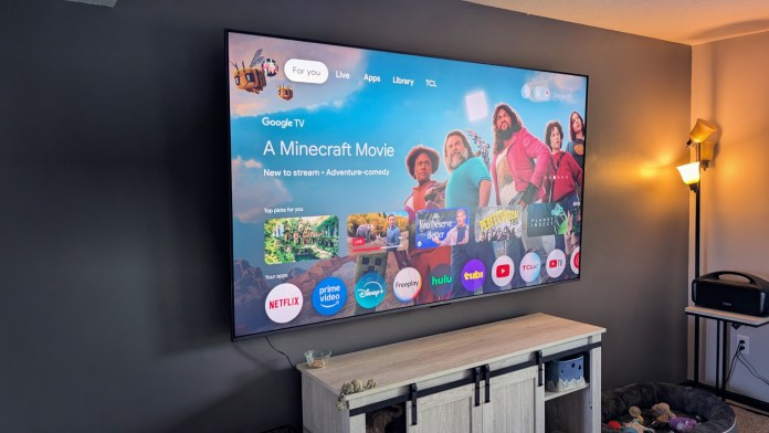 A large TCL 85-inch TV displaying the Google TV interface with a highlighted title 'A Minecraft Movie' and various app icons like Netflix, Prime Video, and Disney+.