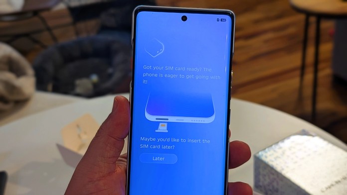 A close-up of a smartphone displaying a setup screen indicating readiness for SIM card insertion, held in a person's hand, with a soft-focused background.