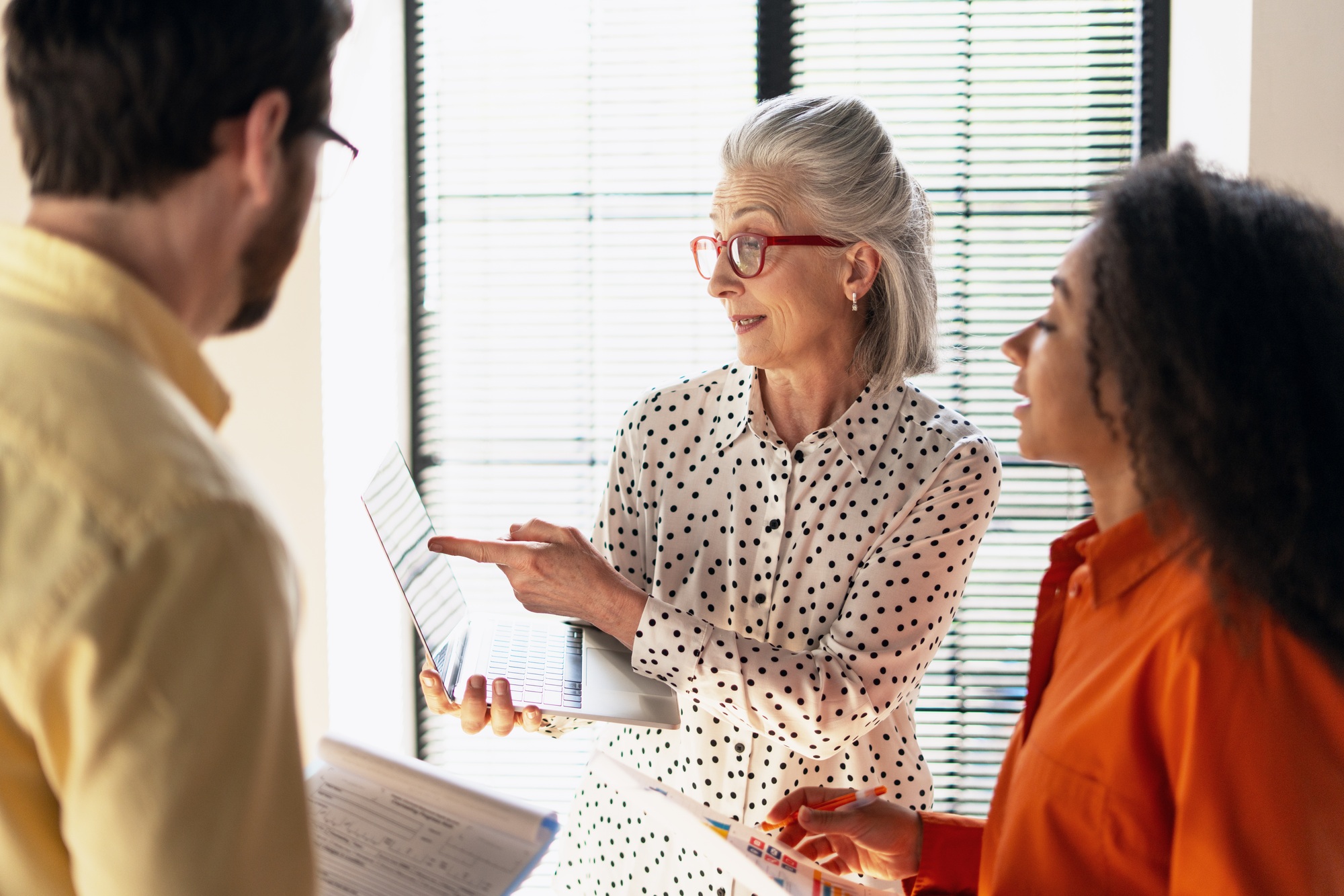 Senior businesswoman pointing at laptop screen showing project statistics to colleagues