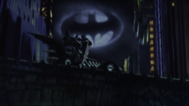 Val Kilmer's Batman swings into the foreground with the batmobile and bat signal in the background in Batman Forever
