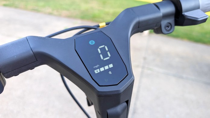 Close-up of a scooter dashboard displaying speed in mph, with various symbols indicating battery level and settings.