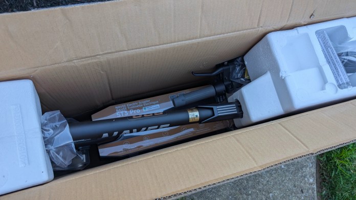 An electric scooter, the Navee ST3 Pro, partially assembled inside its packaging, showing components like the scooter frame and protective styrofoam.