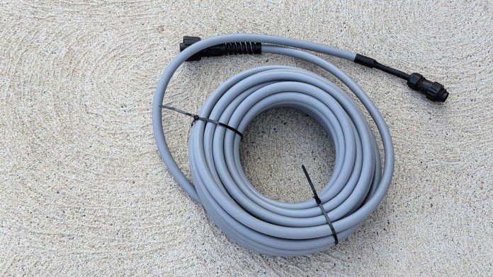 A coiled gray cord or hose with connectors, lying on a textured surface.