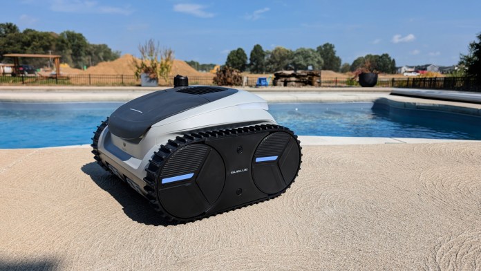 A robotic pool cleaner positioned at the edge of a swimming pool, showcasing its sleek design and robust tracks against a sunny outdoor backdrop.