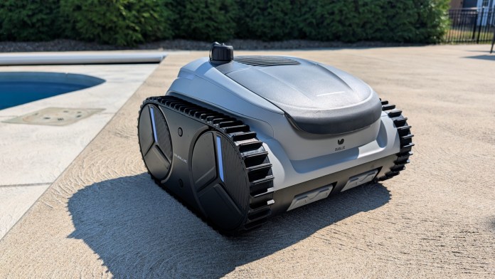 A robotic pool cleaner with a sleek design, showcasing a UV-resistant shell and tank-style tracks, positioned near a swimming pool on a concrete surface.