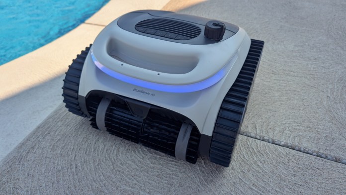 A robotic pool cleaner positioned near the edge of a pool, showcasing its sleek design and BlueSonic AI technology.
