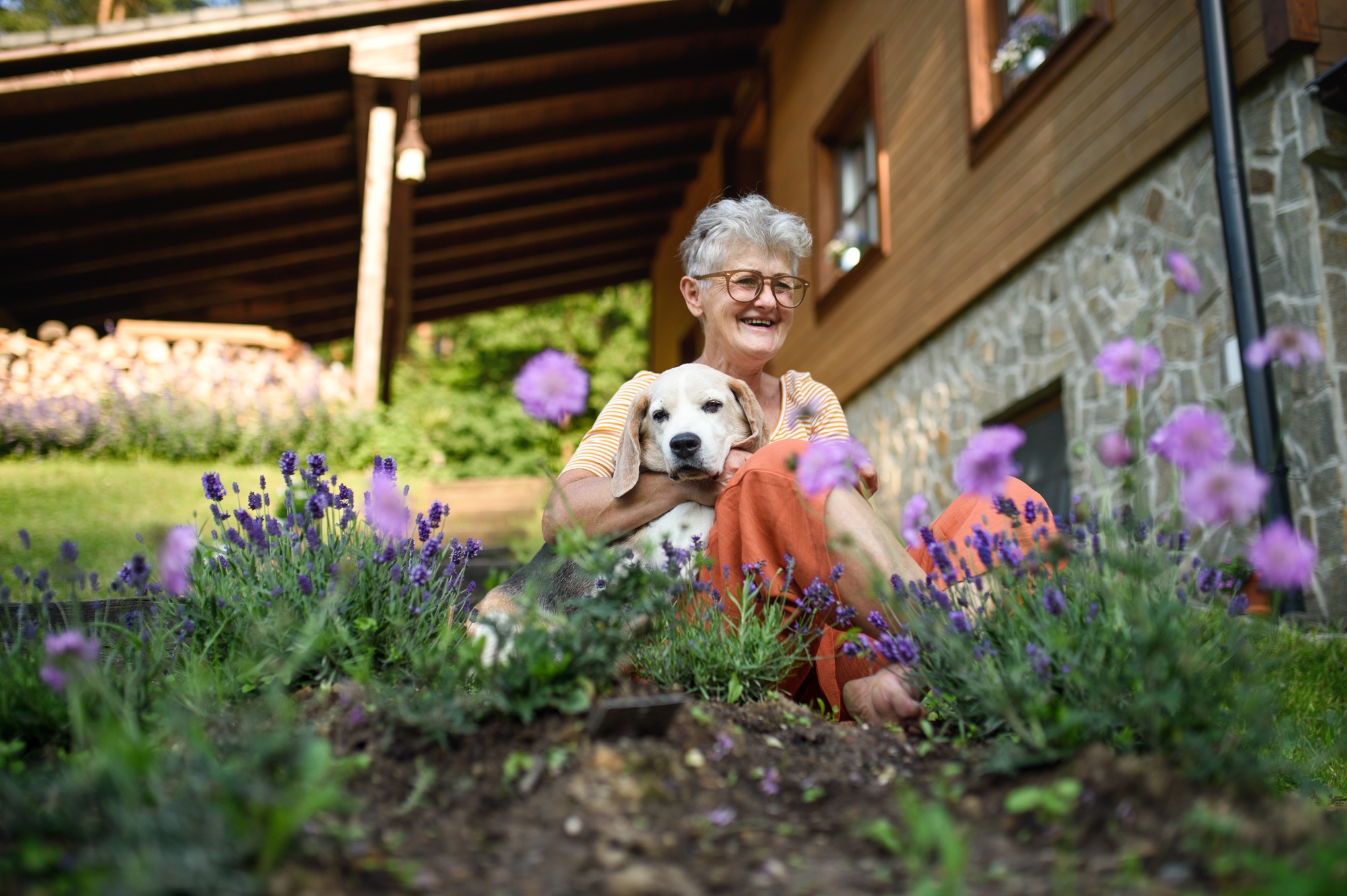 Portrait of senior woman sitting outdoors in garden, pet dog friendship