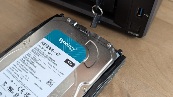 Close-up of a Synology HAT3300 4TB SATA drive being inserted into a NAS with a key visible for locking mechanism.