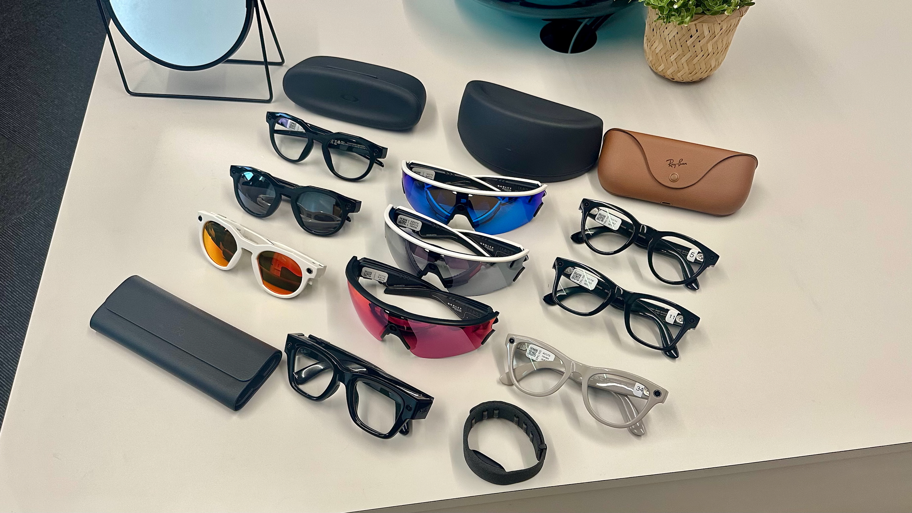 Three Oakley Meta HSTN, three Oakley Meta Vanguard, and three Ray-Ban Meta (Gen 2), along with cases, sitting atop a table in various styles, along with the Meta Ray-Ban Display glasses in front of them all.