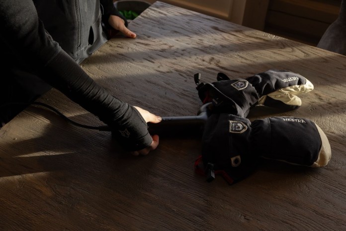 A person using the Hedgehog GO dryer on a pair of gloves, resting on a wooden table.