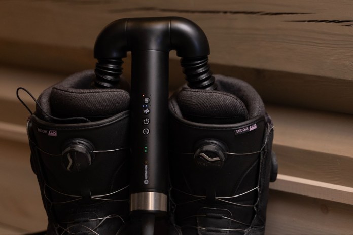 A close-up of the Hedgehog GO dryer attached to a pair of black ski boots, showcasing its compact design and controls.
