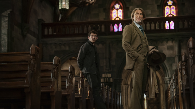 Benoit Blanc and Father Jud stand in a church, looking off camera in Wake Up Dead Man